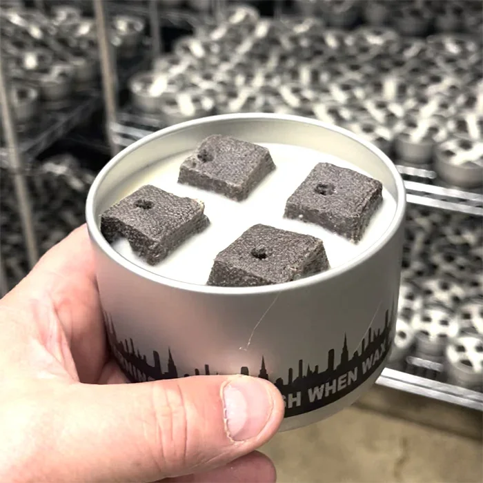 A hand holding an open City Bonfire tin with four briquettes inside