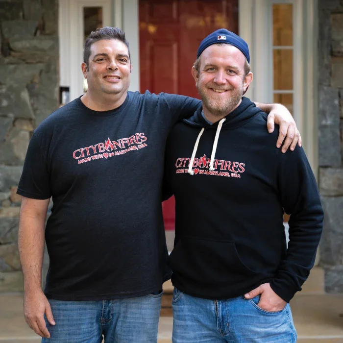 Two men in City Bonfires shirts standing in front of a house